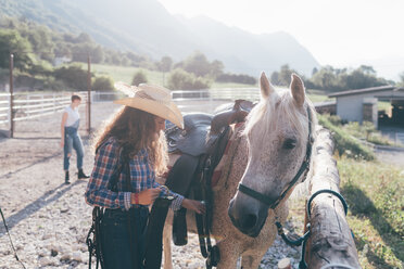 Junges Cowgirl überprüft den Sattel in einer ländlichen Reithalle - CUF47494