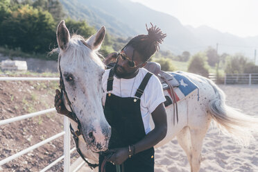 Cooler junger Mann, der sich mit seinem Pferd in einer ländlichen Reithalle anfreundet - CUF47499
