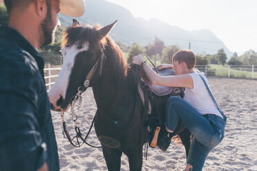 Junge Frau besteigt Pferd in ländlicher Reithalle - CUF47500