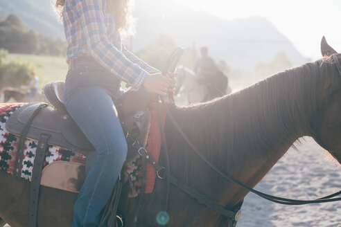 Junge Frau reitet auf Pferd in sonnenbeschienener Reithalle, Ausschnitt, Primaluna, Trentino-Südtirol, Italien - CUF47507