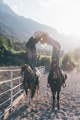 Cowgirl und Freund stehen auf dem Pferderücken und küssen sich in einer Reithalle, Primaluna, Trentino-Südtirol, Italien - CUF47511