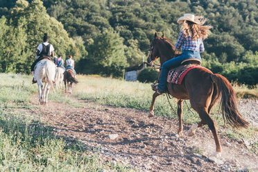 Young adults riding horses in rural landscape, rear view, Primaluna, Trentino-Alto Adige, Italy - CUF47515