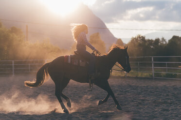 Langhaarige junge Frau galoppiert auf einem Pferd in einer ländlichen Reithalle, Gegenlicht, Primaluna, Trentino-Südtirol, Italien - CUF47523