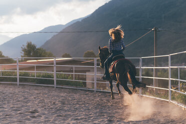 Langhaarige junge Frau galoppiert auf einem Pferd in einer ländlichen Reithalle, Rückansicht, Primaluna, Trentino-Südtirol, Italien - CUF47524