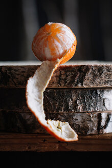 Teilweise geschälte Mandarine auf rustikalem Schneidebrett - CUF47560
