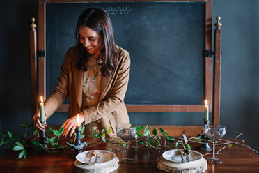 Young woman decorating vintage dinner table with candle and foliage - CUF47588