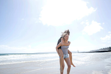 Sisters playing piggyback on beach - CUF47715