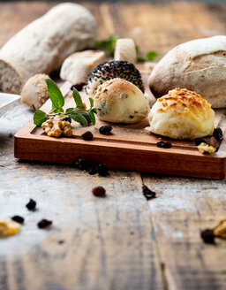 Seeded bread rolls and rustic loaves on chopping board, still life - CUF47833