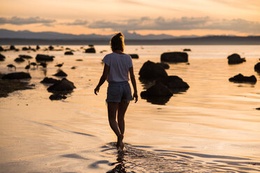Young woman ankle deep in water at sunset, Quadra Island, Campbell River, Canada - CUF47861
