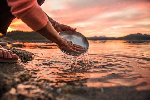 Mature woman washing plate at sunset, cropped, Quadra Island, Campbell River, Canada stock photo