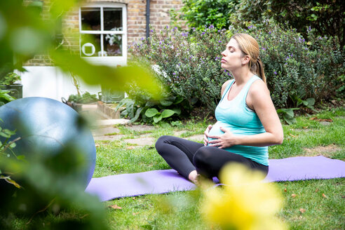Schwangere Frau im mittleren Erwachsenenalter übt Yoga-Meditation im Garten - CUF47878