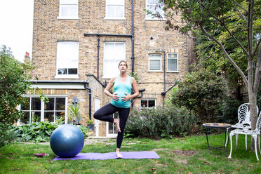 Schwangere Frau im mittleren Erwachsenenalter übt Yoga-Baum-Pose im Garten - CUF47880