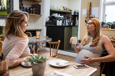Schwangere Frau im mittleren Erwachsenenalter und beste Freundin unterhalten sich bei einem Kaffee im Café - CUF47882
