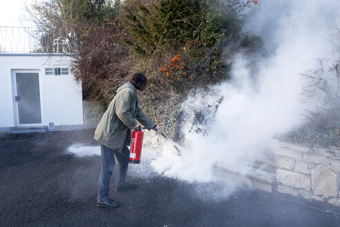 Mann beim Löschen eines Kabelbrandes im Garten neben dem Haus - NDF00854