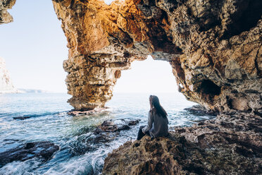 Spain, Alicante, woman sitting on the rocks on the beach of Benitachell - OCMF00212