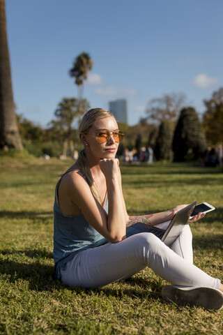 Junge Frau sitzt im Park mit Handy und Laptop, lizenzfreies Stockfoto