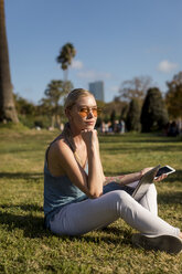 Young woman sitting in park with cell phone and laptop - MAUF02300