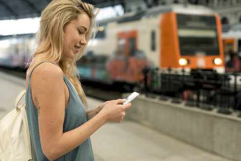 Lächelnde junge Frau beim Telefonieren am Bahnhof - MAUF02314