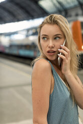 Porträt einer jungen Frau, die am Bahnhof mit ihrem Handy telefoniert und sich umschaut - MAUF02316