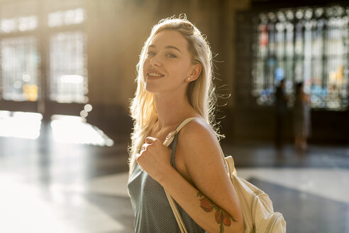 Porträt einer lächelnden jungen Frau mit einer Tätowierung im Gegenlicht - MAUF02322