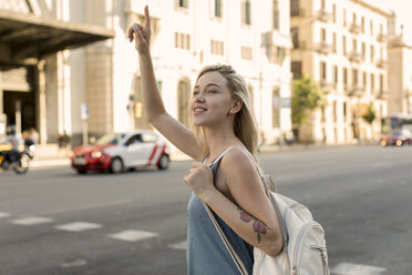 Smiling young woman in the city hailing a taxi - MAUF02323