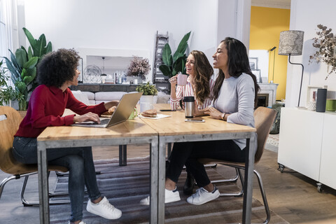 Drei glückliche Frauen mit Laptop am Tisch, lizenzfreies Stockfoto