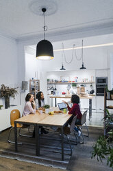 Three women with laptop talking at table - GIOF05478