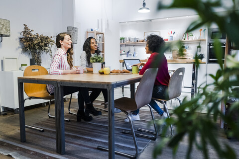 Three women with laptop talking at table stock photo