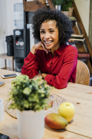 Porträt einer glücklichen Frau, die am Tisch sitzt, lizenzfreies Stockfoto