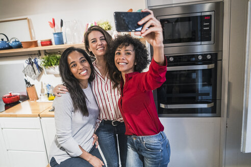 Drei glückliche Frauen posieren für ein Selfie in der Küche - GIOF05487