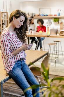 Frau mit Mobiltelefon am Tisch - GIOF05488