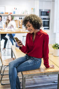 Lächelnde Frau mit Mobiltelefon auf dem Tisch sitzend - GIOF05491