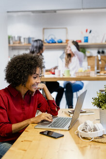 Lächelnde Frau mit Laptop auf dem Tisch - GIOF05494