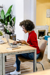 Smiling woman using laptop and cell phone at table - GIOF05498