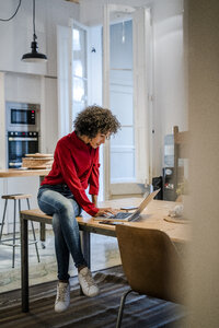 Junge Frau sitzt auf einem Tisch und benutzt einen Laptop - GIOF05499