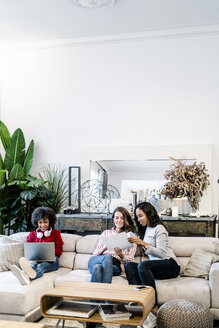 Drei Frauen mit Laptop und Dokumenten auf einer Couch sitzend - GIOF05506