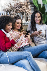 Three smiling women sitting on couch using cell phones - GIOF05507