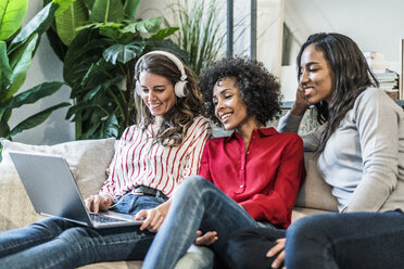 Three happy women with laptop sitting on couch - GIOF05509