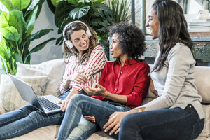 Drei glückliche Frauen mit Laptop auf der Couch sitzend - GIOF05510