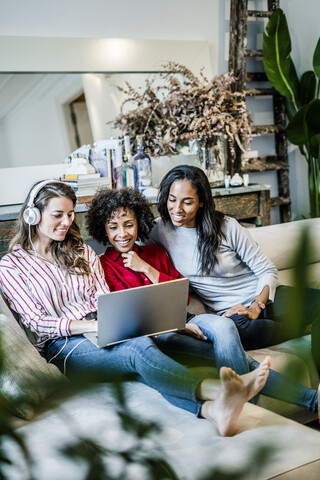 Drei glückliche Frauen mit Laptop auf der Couch sitzend, lizenzfreies Stockfoto