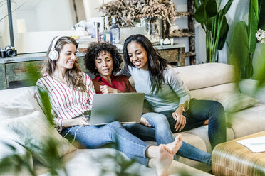 Drei glückliche Frauen mit Laptop auf der Couch sitzend - GIOF05512