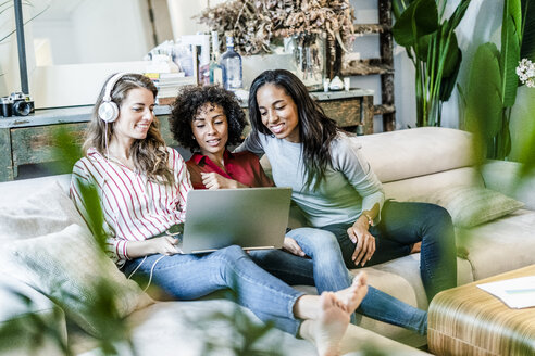 Drei glückliche Frauen mit Laptop auf der Couch sitzend - GIOF05512