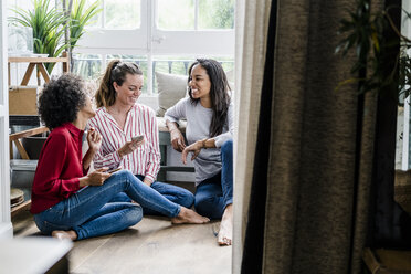 Three happy women sitting on the floor at home with cell phones - GIOF05519