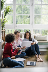 Three women with laptop and documents sitting on the floor at home - GIOF05521