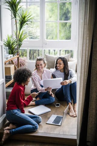 Drei Frauen mit Laptop, Mobiltelefon und Dokumenten, die zu Hause auf dem Boden sitzen, lizenzfreies Stockfoto