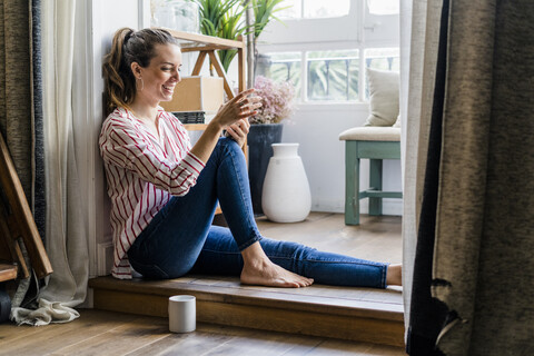 Lächelnde Frau auf dem Boden sitzend zu Hause mit Handy, lizenzfreies Stockfoto