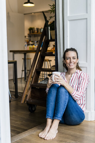 Portrait of smiling woman sitting on the floor at home with cup of coffee stock photo