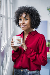 Lächelnde Frau mit einer Tasse Kaffee, die zu Hause aus dem Fenster schaut - GIOF05537