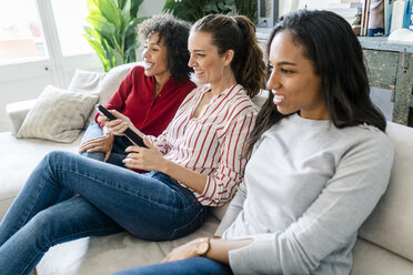 Three happy women sitting on couch at home watching Tv - GIOF05545