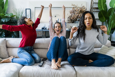 Drei aufgeregte Frauen auf der Couch zu Hause, die fernsehen und jubeln - GIOF05547